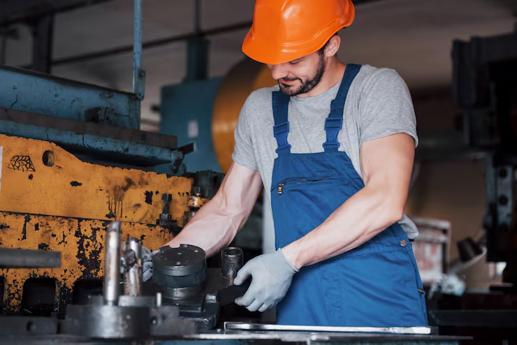 Factory worker in blue overalls and orange helmet operating industrial machinery in a manufacturing setting